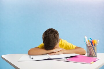 Exhausted child sitting at the table, writing in a notebook, studying