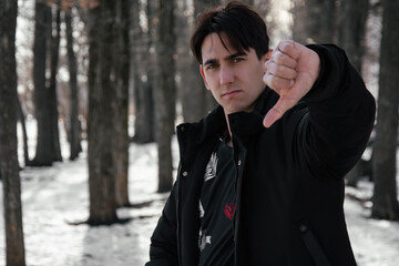 Portrait of a disgruntled man showing thumbs down. The guy is walking on the street.