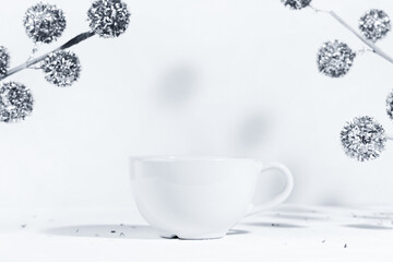 Christmas background with a white ceramic mug with a winter drink, on a white background with Christmas decorations and harsh shadows in the sun.