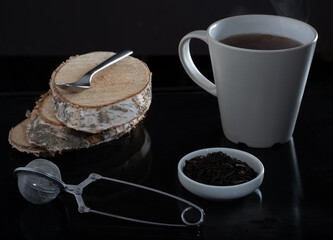 A cup of tea, a cup of fresh tea leaves and a tea strainer