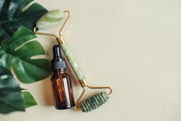 Massage quartz roller for the face of natural nephritis with serum oil with monstera leaves on beige background. © stopabox
