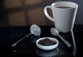 Selective focus closeup of a cup filled with fresh tea leaves. An out-of-focus tea strainer is in the background.