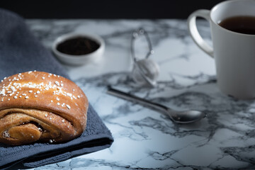 Traditional Finnish cinnamon roll, a teacup and small bowl of fresh tea leaves on a marble table.
