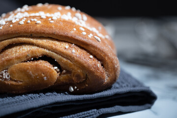 Closeup of a traditional Finnish cinnamon roll on top of a kitchen towel against a black background