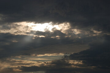Obraz premium Summer cloudy sky covered with clouds. In the sky, white-gray, slightly blue clouds with white gaps through which the sun's rays break through.