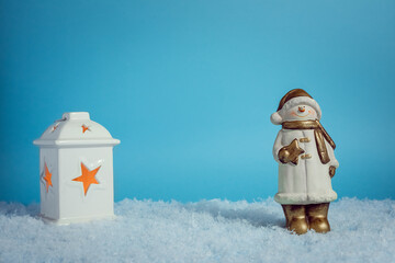 Happy snowman stands on a blue background with a white candlestick in the snow with copy space