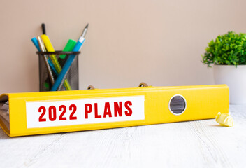A yellow folder labeled 2022 PLANS is on the office desk. Flower and stationery background.