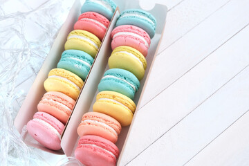 Multicolored macarons in a row on a white wooden background. Concept for a festive look of sweets, cafe, bistro, recipes