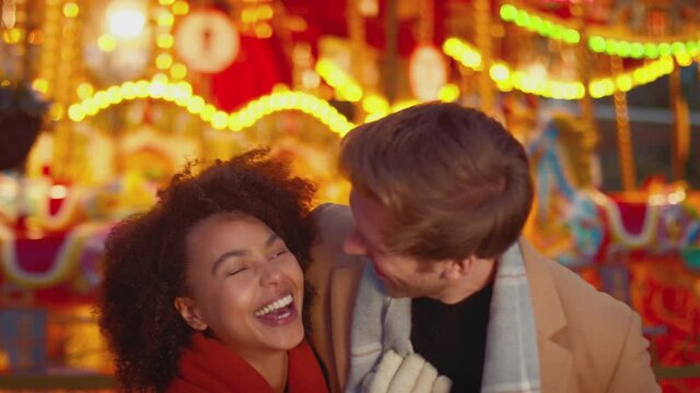 Portrait of couple enjoying on date in standing by carousel at Christmas funfair at night - shot in slow motion