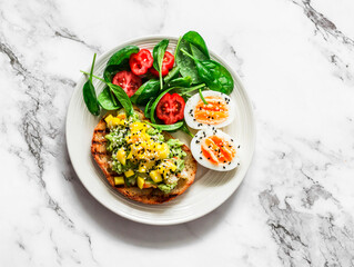 Delicious breakfast, snack - sandwich with avocado, shrimp, mango salsa, boiled egg and spinach tomatoes salad on a light background, top view