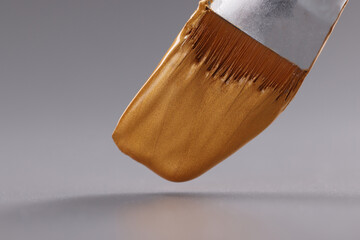 Closeup of brush with gold paint on gray background