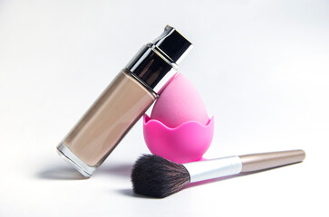 A makeup sponge. Makeup brush and makeup base. Beige liquid foundation for makeup, applied with a...