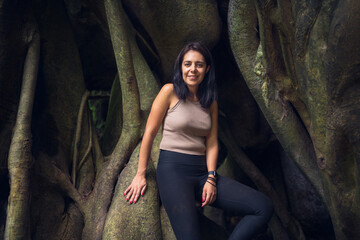 Young woman posing on a giant root tree in the tropical forest. Young woman in green wet forest on sunny day. Sustainable tourism concept. Amatlán, Mexico.