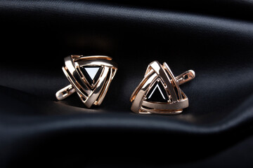 Golden earrings with the black stone on black leather background.