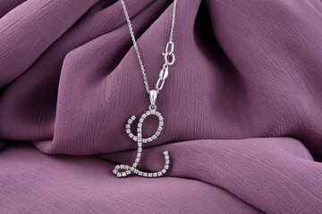 Silver necklace with a diamond pendant on purple fabric background.