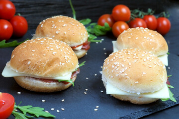 Sesame buns. Ham and cheese burgers on a background of fresh tomatoes and greens