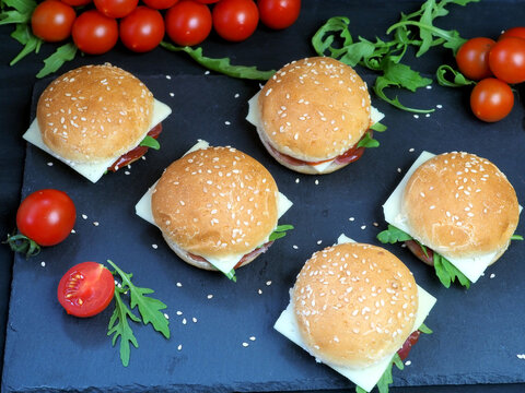 Lots of fresh sandwiches with cheese and ham, herbs, tomatoes. On a black background. Flat lay