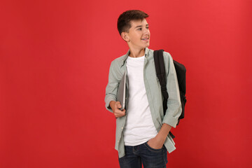 Teenage student with backpack and laptop on red background