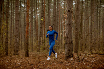 Young woman running on the forest trail at autumn