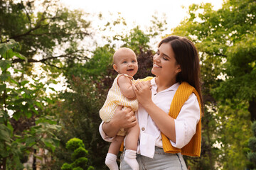 Happy mother with adorable baby walking in park on sunny day, space for text