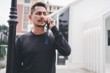 Asian young man standing on the street and looking aside while talking by his phone.