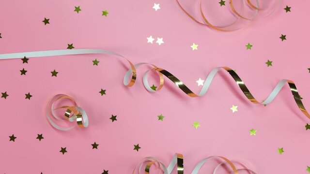 flat composition of gold ribbons or serpentine and gold confetti in the from of stars on a pink background. Concept of a newborn girl or girly birthday or celebration