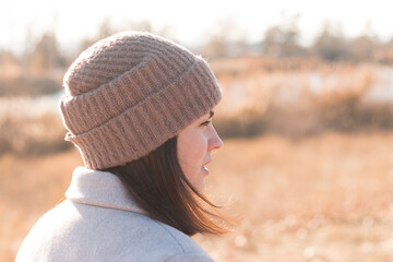 A serious girl in a knitted hat stands against a background and a coat against the backdrop of an...