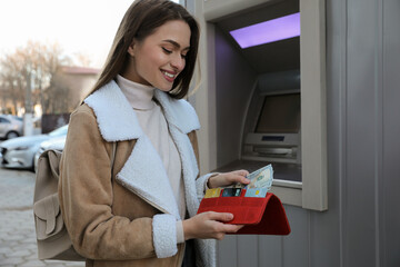 Woman putting money into wallet near cash machine outdoors