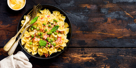 Fettuccine pasta with bacon and green peas and parmesan cheese in old pan on old dark wooden background. Top view.