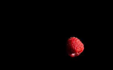 Single fresh raspberry on black background