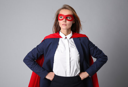 Confident businesswoman wearing superhero cape and mask on light grey background