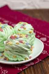 Christmas green mojito flavored marshmallow garnished with multicolored sugar sprinkles on a white saucer and white wooden background. Festively decorated New Year's sweet food. Vertical orientation.