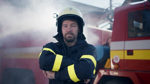 Mature dirty firefighter putting on helmet with fire truck at background