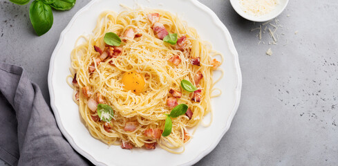 Pasta spaghetti carbonara with bacon, parmesan cheese, egg yolk and basil leaves on gray light background. Traditional Italian dish. Top view.