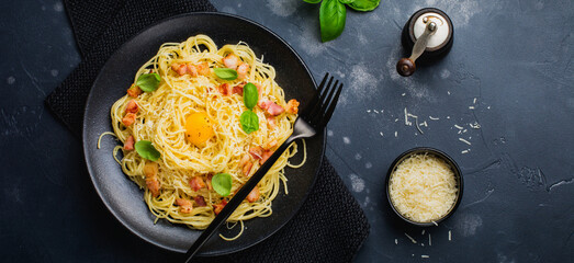 Pasta spaghetti carbonara with bacon, parmesan cheese, egg yolk and basil leaves on black background. Traditional Italian dish. Top view.