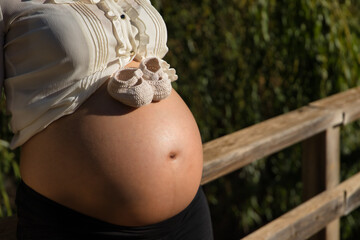 Detail of pregnant woman's belly with baby booties on it, in an outdoor park. Concept pregnancy,...