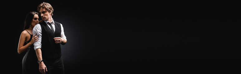 sexy woman in slip dress hugging man in vest and shirt on black, banner.