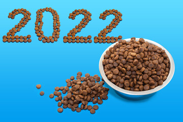 Happy new year for pets. Date 2022 composed of dry food and a round metal bowl full of crunchy dry...