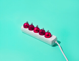 Red Christmas decorations in the extension cord. Festive minimal idea on a blue-green background.
