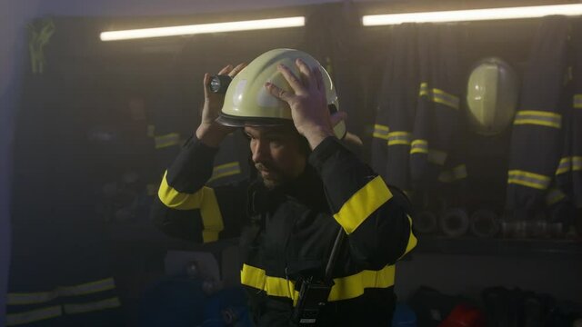 Mature caucasian firefighter putting on helmet indoors in fire station, getting ready for action at night