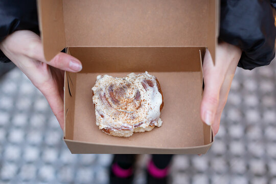 A girl holds a cinnabon with cream in a craft box. Fresh baked goods delivery.