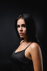 Naklejka premium brunette young woman in slip dress looking at camera isolated on black.