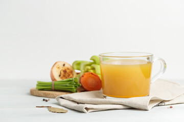 Vegetable or meat broth in a glass mug. Close-up, vegetables and roots in the background.