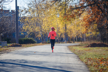 Young fitness woman running on the road in the cold morning in winter. Sporty girl in orange long-sleeve jogging in the sunny morning