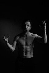 Fototapeta na wymiar Black and white portrait athletic man screams emotionally on a black background.