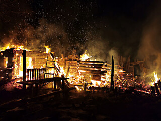 A large wooden building burns at night. Fire blazes and sparks fly. The living room is on fire. Grief and misfortune.