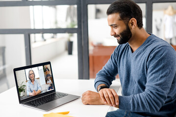 Indian male student studying online, watching webinar holding female teacher, other students involved. Ethnic multiracial man member of video conference, using laptop for connecting online