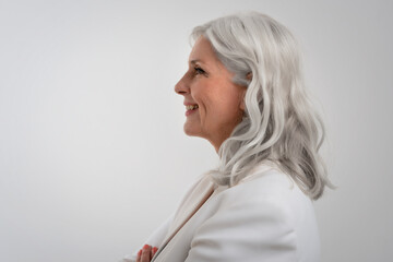 Side view of grey haired senior woman portrait while standing at isolated background