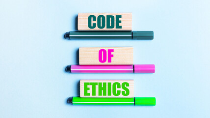 On a light blue background, there are three multi-colored felt-tip pens and wooden blocks with the CODE OF ETHICS