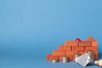 Stacks of coins in the form of steps against a background of red brickwork and a masonry trowel. Construction investment concept